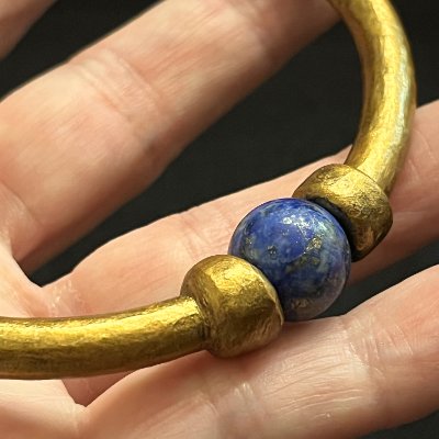 Close-up detail of the authentic spherical lapis lazuli bead threaded into the replica gold bangle.