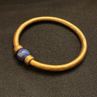 The replica Pharaoh Amenemope gold bracelet resting flat against a dark textured archival background.