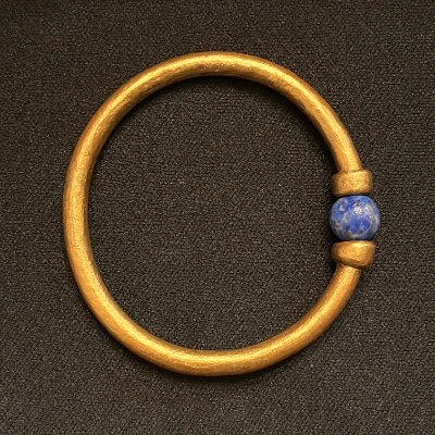 Top-down archival view of the replica 21st Dynasty gold bangle resting on a dark surface.