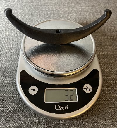 The composite plastic bannerstone replica rests on a digital scale displaying its 32-gram weight.