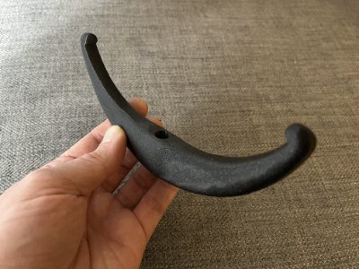 A hand holds the black lunate bannerstone replica to display its curved profile and central hole.