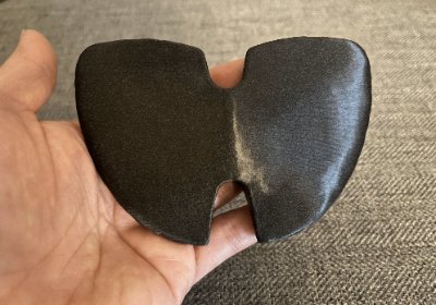 Dorsal view of the dark composite winged bannerstone replica resting flat in a handler's palm.