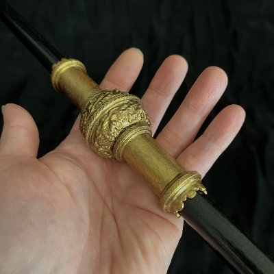 Hand holding the central collar of the replica staff to demonstrate scale.