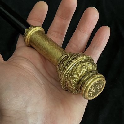Hand holding the base of the replica Black Rod showing golden patina and metal replica 1904 British Sovereign. 