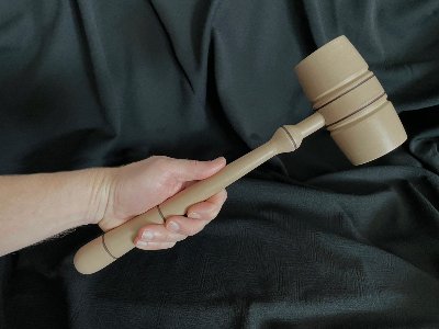 Hand holding the replica wood gavel horizontally against a dark fabric background for scale.