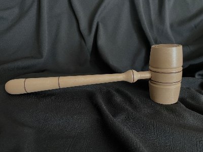 Wood replica of the United States House of Representatives gavel resting horizontally on dark fabric.
