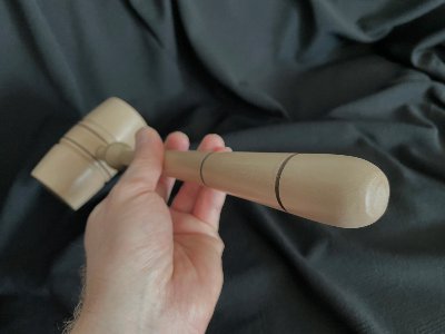 Hand gripping the replica gavel at a slight downward angle to highlight its balanced weight.