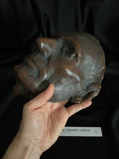 Low angle profile view of the mask held by hand against a dark background.