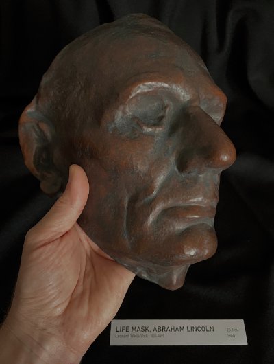 Three-quarter right profile of the life-size mask held in hand to demonstrate scale.