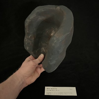 A hand reveals the hollow interior construction of the cast limestone replica mask.