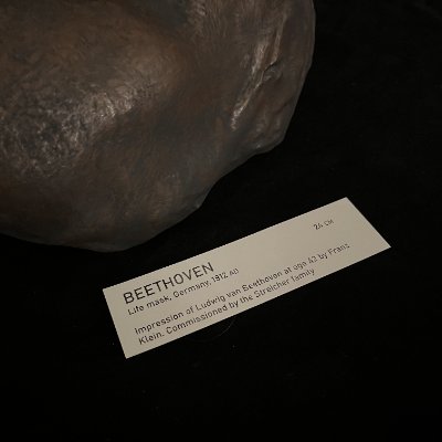 A close-up focuses on the accompanying museum display tag identifying the 1812 mask.