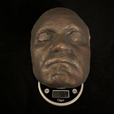 The life-size replica mask rests on a digital scale to document its overall weight.
