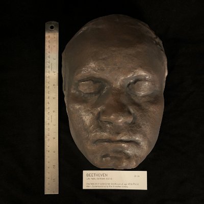 The replica mask sits vertically beside a metal ruler showing 24 cm height.