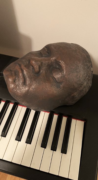 The dark finished replica life mask rests face-up across the keys of a piano.