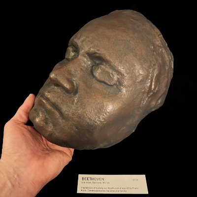A hand elevates the replica mask to exhibit its three-quarter profile and patina.