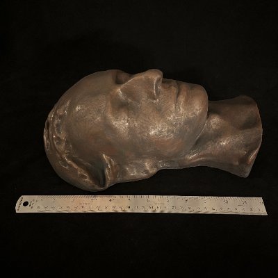 Left profile of the mask displayed lying flat alongside a wooden ruler.