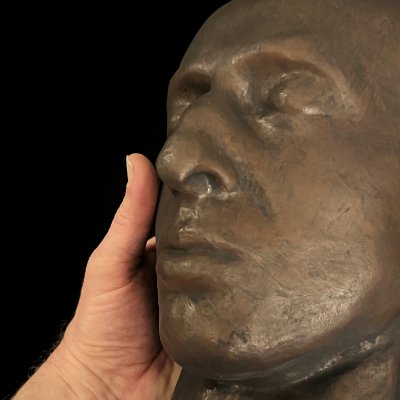 Close-up of the right facial profile held by hand, showing the bronze finish.