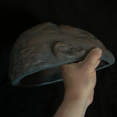 A hand holds the effigy to display the lateral edge and hollow internal structure.