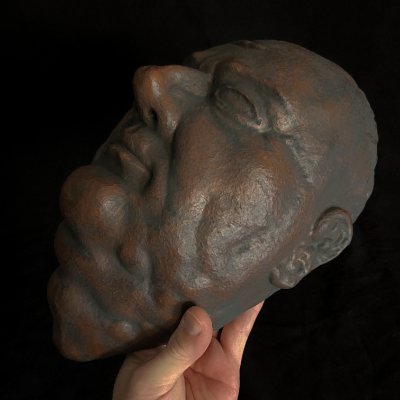 A hand supports the mask to exhibit the right lateral facial profile.
