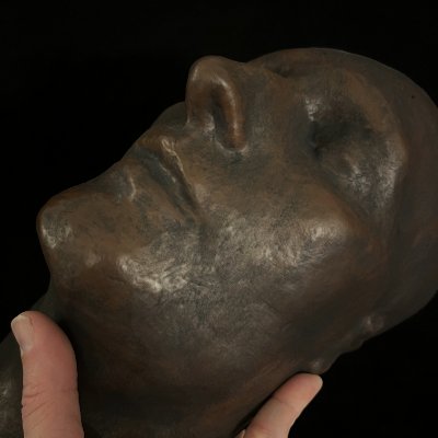 Close-up low angle view of the facial contours and bronze patina of the held replica.