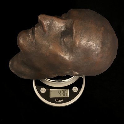 The 1821 Napoleon death mask replica resting flat upon a digital scale to show weight.