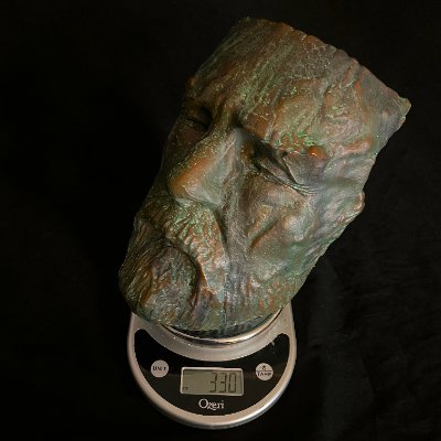 Face mask replica resting on a digital scale displaying a weight of 330 grams.