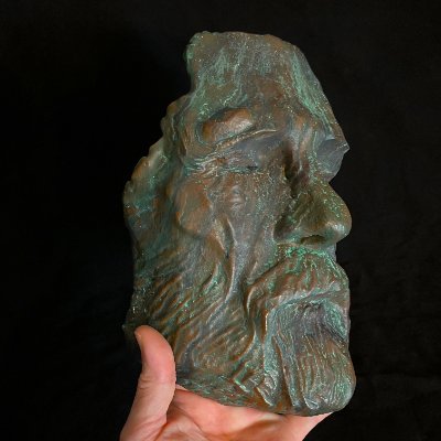 Right profile view of the face mask replica held upright by a hand.