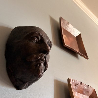 Angled view of the bronze-toned mask mounted among wall art pieces.