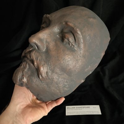 A hand supports the mask replica, highlighting the left facial profile.