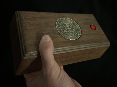 A hand grips the replica call box from the side, demonstrating its scale and substantial build.