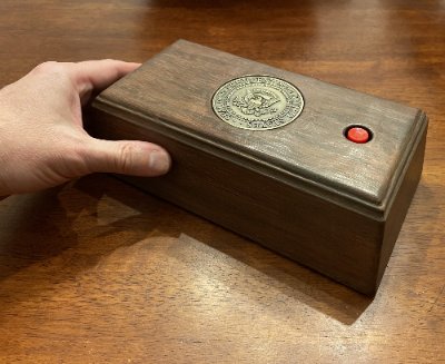 The wooden Presidential call box replica resting on a wood grain surface, with a hand for scale.
