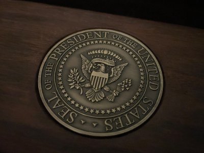 Detailed macro photograph of the heavy, detailed bronze Seal of the President on wood grain.