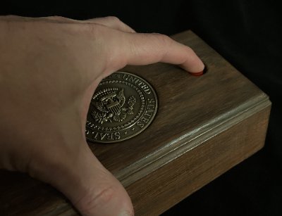 A finger presses the industrial-grade functional red momentary switch on the wooden call box.