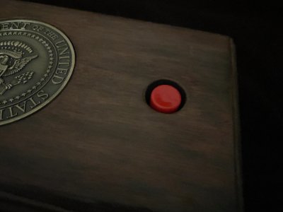 Detailed close-up view of the red momentary switch and the edge of the bronze Seal of the President of the United States.