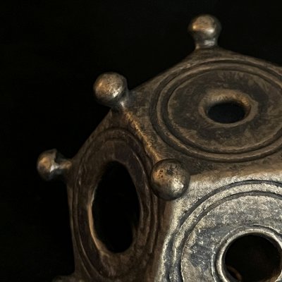 Macro photography reveals the hand-worked bronze patina, corner knobs, and circular face aperture.