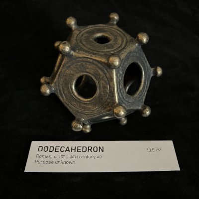 Angled view of the Roman dodecahedron replica presented alongside its accompanying museum label.