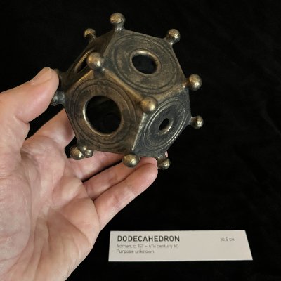 The artifact replica is held above its descriptive exhibition label to illustrate its relative size.