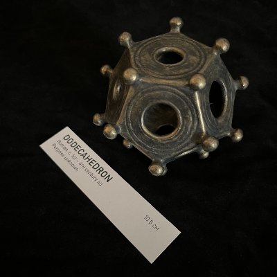 The geometric bronze-finished replica rests near a diagonally placed museum reference card.