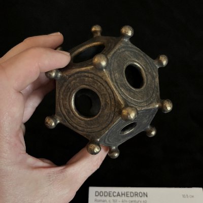 A side profile of the Roman dodecahedron replica supported by a human hand for dimensional context.
