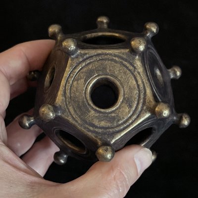 Fingers grip the knobby exterior of the 12-sided Roman artifact replica to show its tactile qualities.