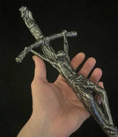 Hand cradling the center of the crucifix to display the scale and sculptural detailing.