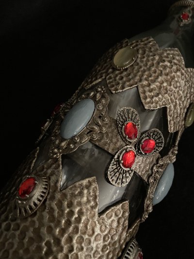 Detailed look at a large pink cabochon bordered by textured metallic trim on the glass bottle.