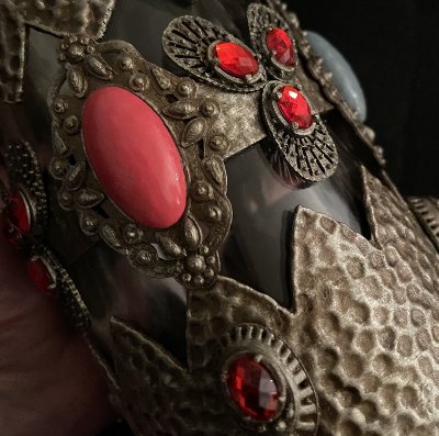 Macro shot of the hammered overlay detailing the setting of red rhinestones and a pink cabochon.