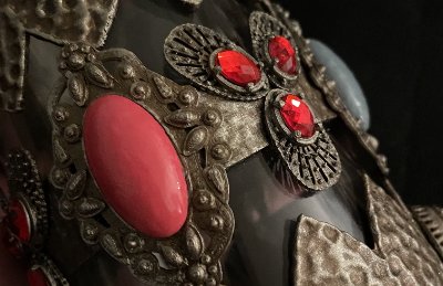 Close-up detail of textured metallic overlay featuring a large pink cabochon and red rhinestones.