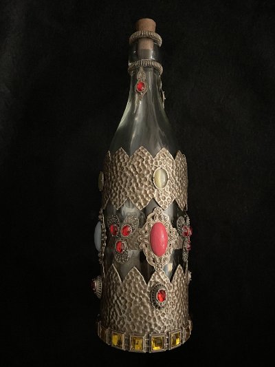 Full upright view of the ornate glass theatrical wine bottle against a black background.