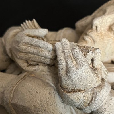 Extreme close-up of the carved hands and book highlighting the limestone patina.