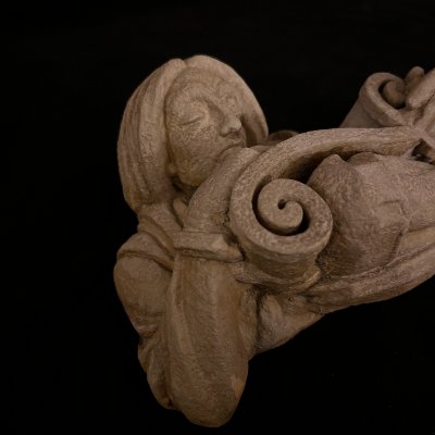 Detailed angled view of the carved hands unrolling the curled gothic scroll element.