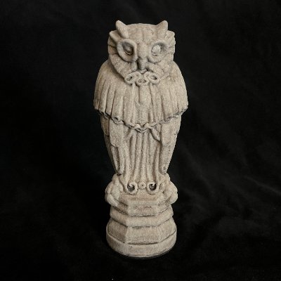 Frontal view of the limestone Yale Law School owl sculpture against a dark background.